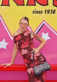 Bordeauxrotes Blumenkleid mit geraffter Textur und kurzen Ärmeln. Schwarze Handtasche mit Blumenmuster. Heller, farbenfroher Hintergrund.