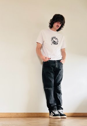 Camiseta blanca con un diseño gráfico negro, combinada con jeans de mezclilla negros holgados que presentan detalles desgastados, y zapatillas en blanco y negro.