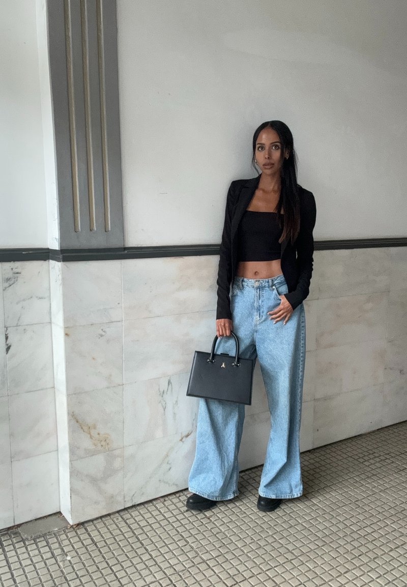 Μαύρο εφαρμοστό σακάκι, μαύρο κροπ τοπ, ανοιχτό μπλε παντελόνι με φαρδιές γραμμές και μια μικρή μαύρη τσάντα με χερούλια. Λείες υφές, κα Casual στυλ.