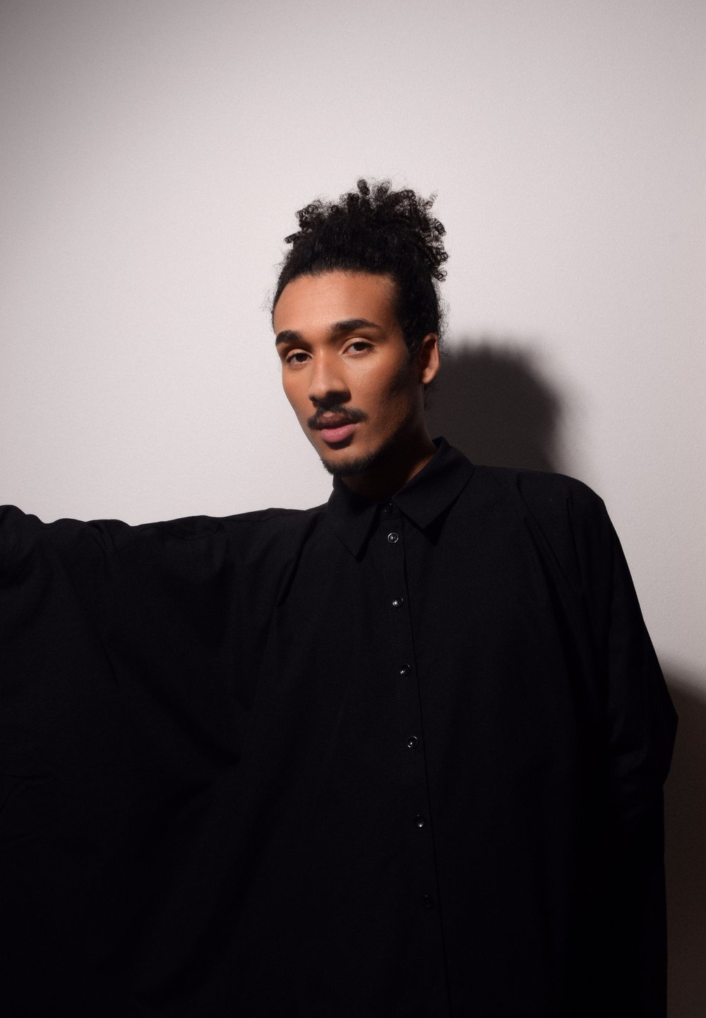 Chemise noire oversize en tissu lisse, avec un devant à boutons, un col pointu et des manches larges. Fond gris clair.