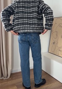 Svart-hvitt rutete flanelljakke over blå jeans med rett snitt. Jeansene har et brodert design på baklommene. Sorte sko.