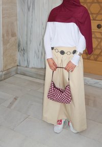 Długa beżowa spódnica z postrzępionym dołem, biała koszula z długim rękawem, bordowa chustka na głowę, szary pasek z okrągłymi akcentami oraz w kratkę bordowa torba.
