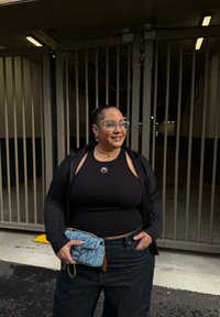 Top nero senza maniche, jeans scuri a vita alta e una borsa di denim con trama e catena. Accessori: occhiali e una collana di perle.