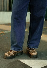 Scarpe con piattaforma in stampa leopardata e suola nera spessa, abbinate a jeans in denim blu scuro a vestibilità ampia. Tessuto testurizzato e design casual.