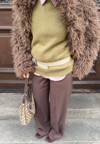 Cappotto marrone peloso, maglione lavorato a maglia verde oliva, camicia rosa chiaro a righe, cintura beige, pantaloni marroni a gamba larga, scarpe bordeaux, borsa a quadri.