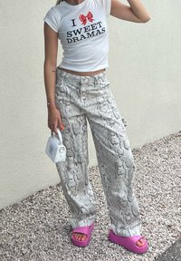 White t-shirt with black text and a red bow, teamed with grey wide-leg trousers featuring a snake print. Pink platform sandals and a white handbag finish off the look.