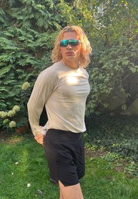 Sportlik pikka varrukaga pehme tan värvi tee, millel on vormiv kujundus ja peened tekstuurid; kaasas mustad lühikesed püksid ja peegeldavad prillid.