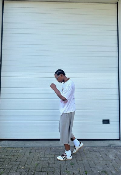 Camisa blanca de manga corta con gráfico rosa, pantalones cortos grises hasta la rodilla y calcetines blancos combinados con zapatillas crema de rayas marrones.