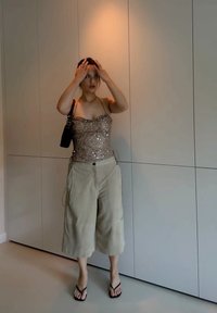 Smešak smešak s metalnim stanicama, upari se s svjetlo bež hlačama širokih nogavica. Crna torba i japanke upotpunjuju odjevnu kombinaciju. Neutralna pozadina.