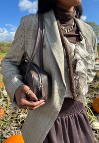 Beige checked blazer, brown turtleneck, frilled white blouse, brown handbag, and brown skirt with a smocked waist; layered accessories are visible.