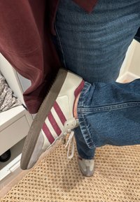 Jasnoszary sneaker z bordowymi paskami, gumową podeszwą i tekstylną cholewką. Noszony z niebieskimi dżinsami, prezentujący swobodny wygląd.