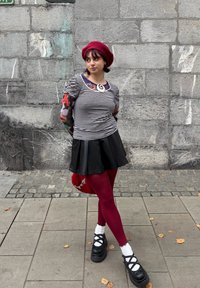 Čierne platformové topánky s krížovými remienkami, bordové legíny, čierna kožená sukňa, pruhované tričko a červený baretk. Pozadie s dlaždicami metra.