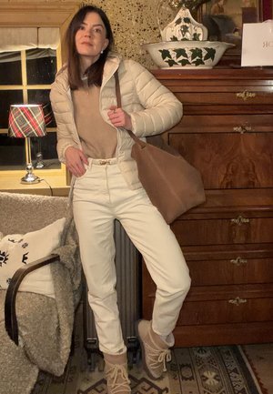 Chaqueta acolchada ligera en crema, suéter beige, pantalones de vestir blancos de talle alto, bolso marrón claro y calzado beige, ambientado en un interior acogedor.