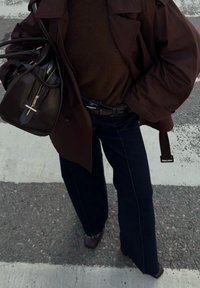 Brun oversized jakke over en brun genser, kombinert med mørkeblå vide jeans. En brun veske med gulldetaljer holdes i den ene hånden.