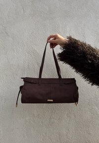 Rjav tkaninski ročni torbica s pravokotno obliko, ki ima dva zgornja ročaja, zlat odtenek in stranske vrvice za širitev.