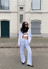 Λευκή φούτερ μπλούζα πάνω από ένα μοτίβο τοπ, συνδυασμένη με ανοιχτό μπλε ριγέ παντελόνια φαρδιάς γραμμής και μαύρα παπούτσια, όρθια σε μια πλακόστρωτη οδό.