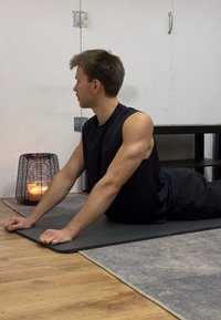 Un top da allenamento nero e pantaloni corti neri su un uomo in posizione cobra su un tappetino da yoga grigio. Una candela accesa in un cestino di metallo è nei dintorni.