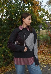 Šedý a burgundský sveter s argyle vzorom cez ružovú pruhovanú košeľu s golierom, v kombinácii s svetlo modrými džínami a hnedou kabelkou.