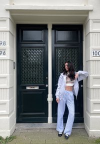 Γκρι φούτερ με φερμουάρ, λευκό κοντό τοπ με γραφικά, ανοιχτό μπλε πουδραρισμένα παντελόνια με λωρί�δες, μαύρα παπούτσια, μπροστά από σκούρες πράσινες διπλές πόρτες.