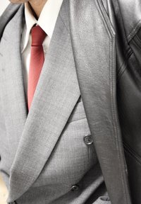 Costume à carreaux gris à double boutonnage, souligné par une cravate rouge et une veste en cuir noir texturée posée sur une épaule.