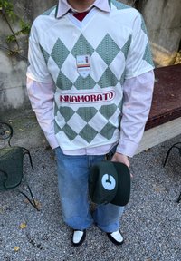 Bela in zelena jersijska majica s diamantskim vzorcem ter grbom in logotipom "INNAMORATO"; v kombinaciji z modrimi kavbojkami in zeleno kapo s belim logotipom.