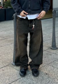 Σκούρο, φαρδύ τζιν παντελόνι με ξεθωριασμένο φινίρισμα, που διαθέτει μπρελόκ με κλειδιά. Φορεμένο με λευκή μπλούζα σε αντίθεση και μαύρα παπούτσια.