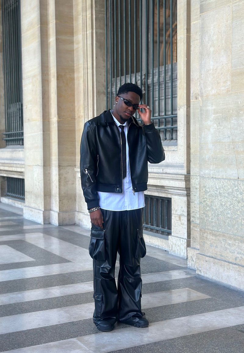 Črno usnjeno bomber jakno, bela srajca, črne cargo hlače z žepi in črni čevlji. Izgled dopolnjujejo označena sončna očala.