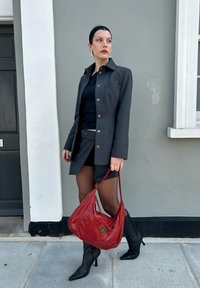 Γκρι σακάκι σε μέτρια εφαρμοστή γραμμή πάνω από μαύρο τοπ, συνοδευόμενο από αντίστοιχες βερμούδες και διάφανα καλσόν. Συνδυάζεται με κόκκινη δερμάτινη τσάντα και μαύρες μπότες με ψηλό τακούνι.