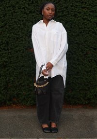 Duża biała koszula zapinana na guziki z kieszenią na piersi, w połączeniu z ciemnymi, luźnymi dżinsami i czarnymi płaskimi butami. Do tego mała czarna torebka z łańcuszkiem.