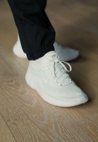 Witte atletische sneakers met een ademend mesh, voorzien van een gedempte zool, een afgeronde neus en witte veters, gecombineerd met zwarte broek met elastische boord.