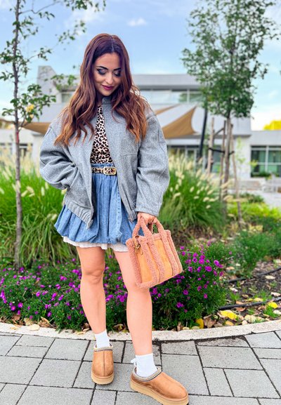 Chaqueta bomber gris de gran tamaño, blusa de leopardo, falda de mezclilla acampanada, bolso texturizado rosa, zuecos marrones, calcetines blancos, fondo floral.