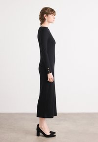 Zwart lange mouwen jurk met een getailleerde silhoet, voorzien van gouden knopenaccenten op de mouwen en een midi-lengte. Draag met zwarte hoge hakken.