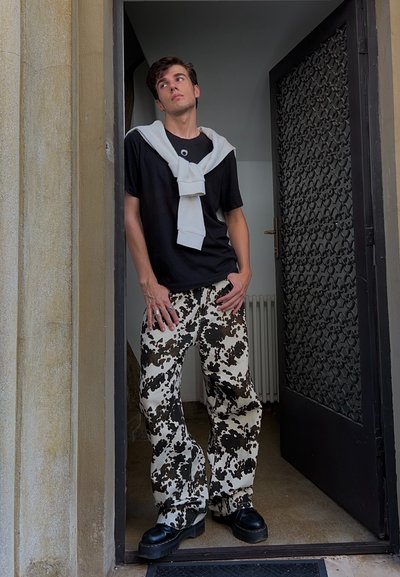 Camiseta negra con un suéter blanco atado al cuello, combinado con pantalones de pierna ancha con un patrón de vaca en blanco y negro y zapatos negros gruesos.