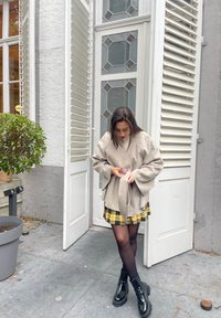 Ανοιχτό γκρι τοπ σε στυλ περιτυλίγματος με φαρδιά μανίκια, συνδυασμένο με κίτρινη καρώ φούστα. Μαύρες παλτό ankle μποτ και διάφανες μαύρες καλσόν ολοκληρώνουν την εμφάνιση.