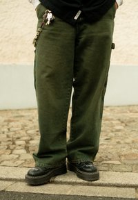 Groene cargobroek met zijzakken, gestructureerde stof, relaxte pasvorm. Zwarte schoenen met een gestructureerde zool en decoratieve stiksels. Sleutels bevestigd.
