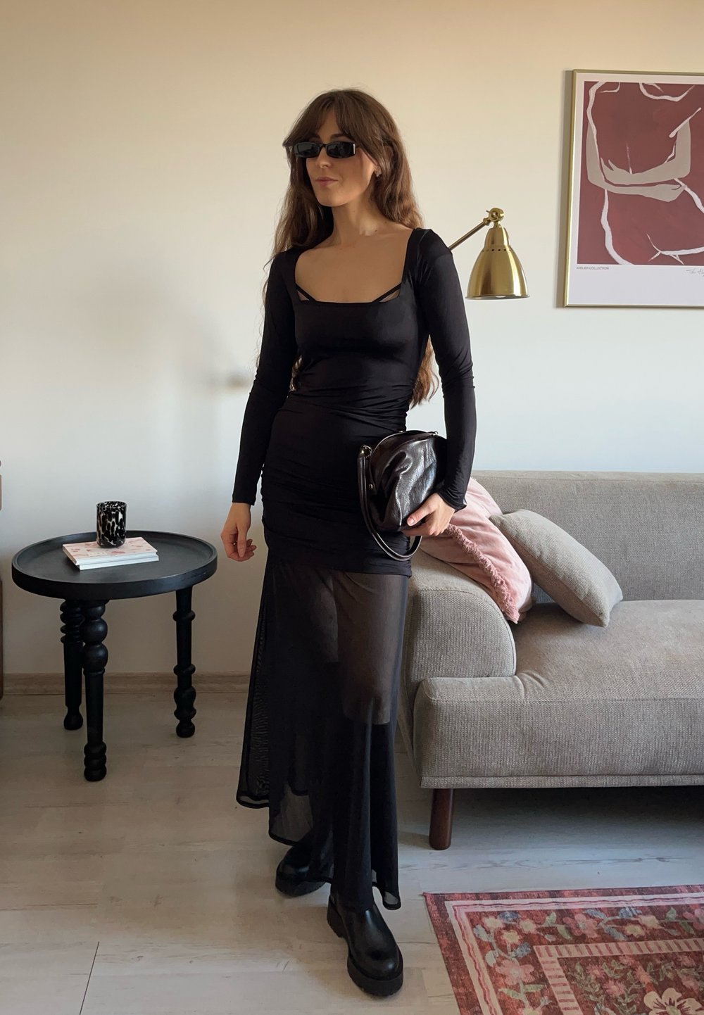 Melnas, garām piedurknēm kleita ar kvadrātveida izgriezumu, rāpja tekstūra, caurspīdīga svārku daļa, kombinēta ar melniem masīviem zābakiem un melnu somu.