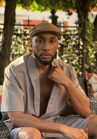 Ανοιχτό γκρι, κοντομάνικο μπουρνούζι με ανοιχτό μπροστινό μέρος, φορεμένο πάνω σε γυμνό δέρμα. Καπέλο σε τόνο καφέ. Φυσικό περιβάλλον με πράσινα φυτά και διακοσμητικά μαξιλάρια.