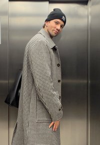 Hundetannmønster frakk i svart og hvitt, med store knapper, krage og sidelommer, kombinert med en svart lue og veske.