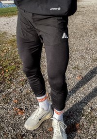 Crne sportske hlače uskog kroja, uparene s uskim crnim helankama. Bijele sportske tenisice s sivim detaljima i narančastim logotipima brenda.