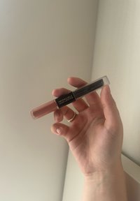 Rossetto Infallible 24HR esposto in una mano. Il tubetto è trasparente con un liquido rosa e un applicatore a pennello nero.