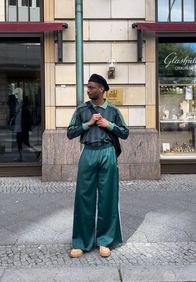 Chándal verde con rayas verticales y pantalones de pierna ancha a juego. Combinado con una boina negra y un bolso de bandolera. Calzado beige.