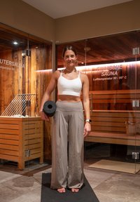 Naissoost spordirõivais naine hoiab musta raskust, seistes mati peal klaasukste ees, millel on sildid "Finnische Sauna" ja "Infrarotsauna".