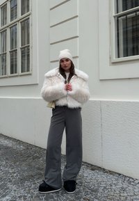 Φουντωτό, λευκό κοντό παλτό με φαρδιά μανίκια, σε συνδυασμό με γκρι ριγέ παντελόνια με φαρδιά πόδια και μαύρες πλατφόρμες. Ζεστό αξεσουάρ καπέλο από πλέξιμο.