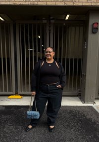 Top corto nero a coste, giacca nera oversize, jeans scuri a vita alta e ballerine nere. Porta una borsa trapuntata azzurro chiaro.