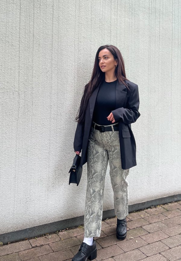 A black blazer worn over a black top, paired with beige snake-print wide-leg trousers. The outfit is completed with black chunky loafers and a small black handbag.