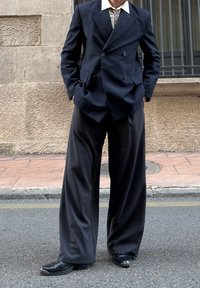 Tamsiai mėlynas dvieilis švarkas su siaurais dryžiais ir plačiomis atvartomis, derinamas su laisvo kirpimo pilkomis kelnėmis ir juodais vienodo batais.