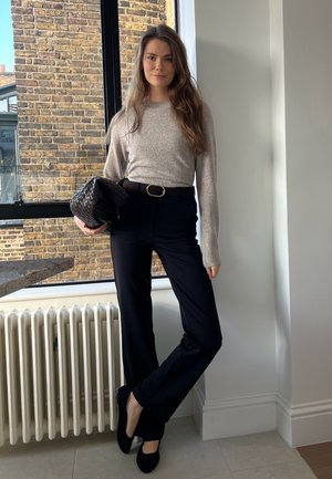 Suéter de manga larga gris claro, pantalones negros, bailarinas negras, clutch trenzado marrón, cinturón fino con hebilla redonda. Texturas suaves y ajuste entallado.