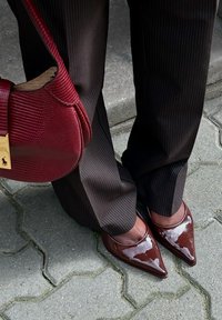 Bruna lackläderskor med spetsig tå i kombination med randiga byxor och en texturerad bordeauxväska med guldaccent.