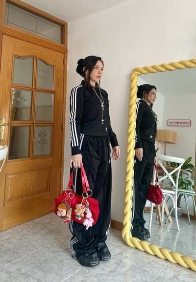 Chándal negro con rayas blancas, bolso rojo con acentos de charm. Textura suave, corte relajado. Espejo reflectante con marco retorcido.