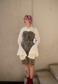 Leopardprint overall med flagrende hvide ærmer og et sort bælte; parret med røde sokker og sorte sko. Accentueret med perlehalssmykke og farverigt hår.